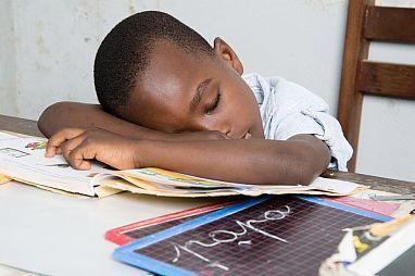 Child sleeping with head down on a desk as school