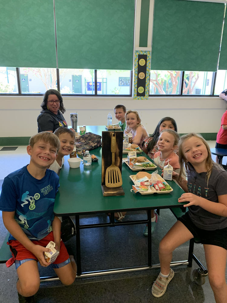Students eating lunch at a table in the cafeteria with a teacher. 